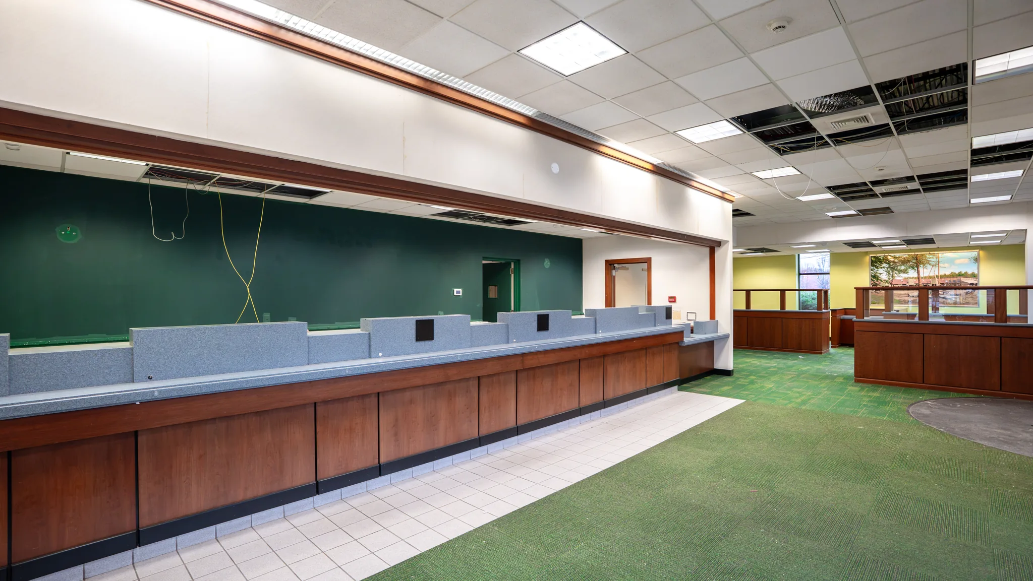 Former bank branch lobby before renovation, with dark green wall, wood teller line, and exposed ceiling wiring