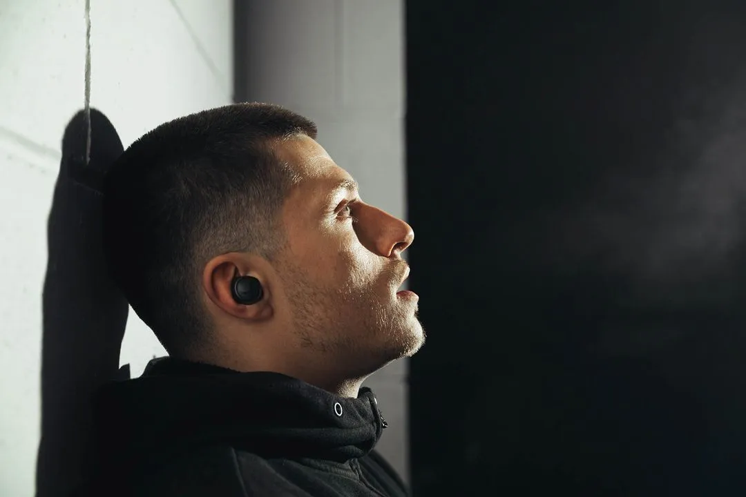 Athlete resting against a wall wearing an earbud