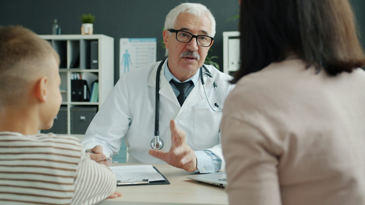 A senior doctor consulting with a young patient and parent, representing patient-centered care and operational excellence in provider practices.