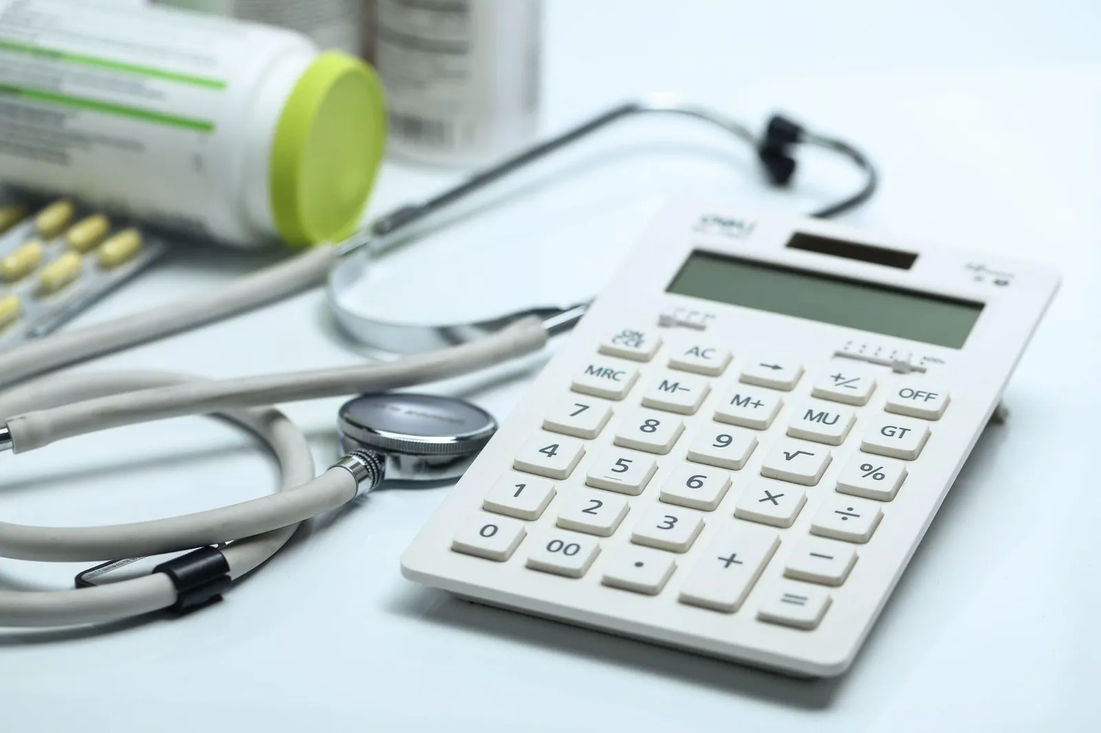 Stethoscope and calculator on a white desk beside medication, representing financial KPIs and performance tracking for a medical practice.