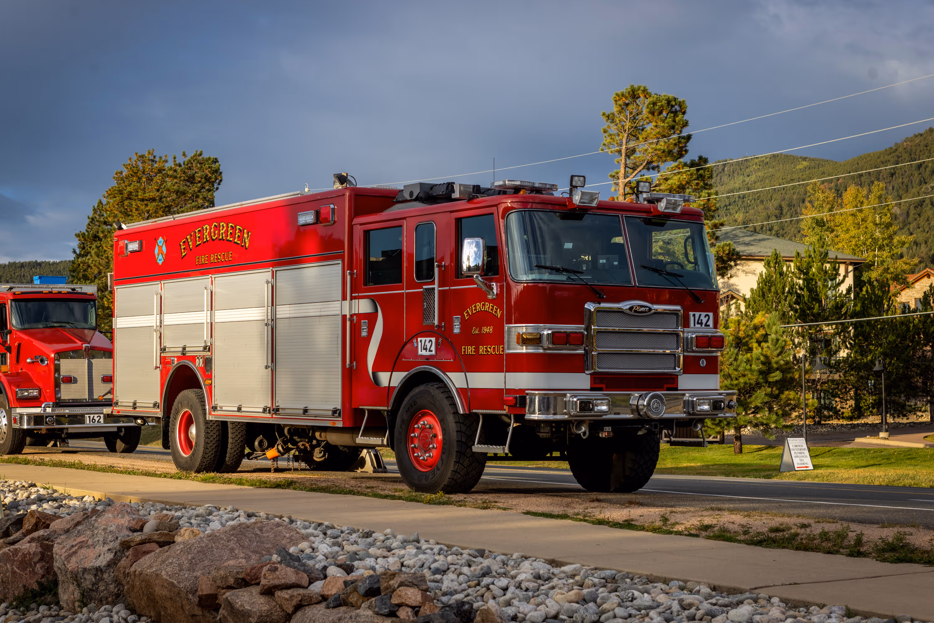 Red Evergreen Fire Rescue fire truck parked on a road near a sidewalk with rocks and trees in the background.