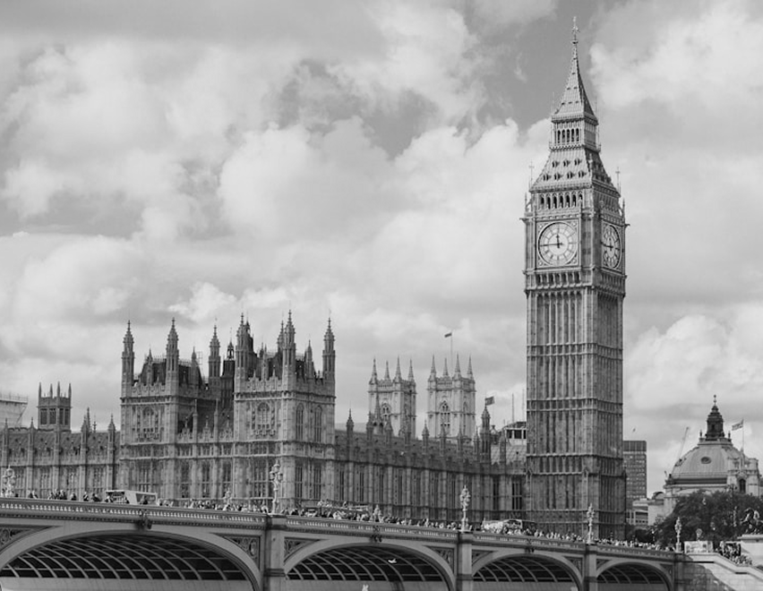 Black and white photo of the Palace of Westminster and Big Ben clock tower in London with a bridge in the foreground.