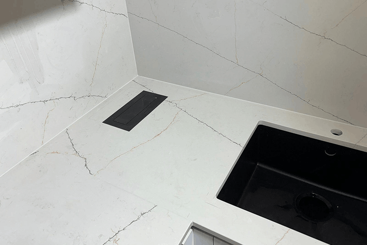 Modern kitchen countertop with white marble surface featuring subtle veins, a black rectangular sink, and a black built-in cooktop.