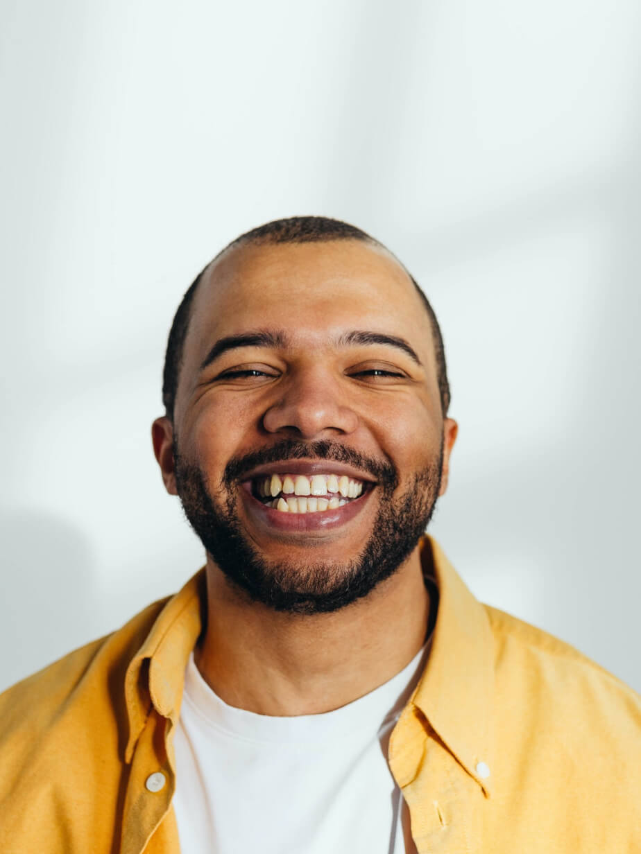 Smiling man with a beard wearing a yellow shirt over a white t-shirt against a light background.