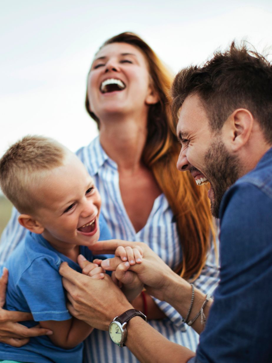 Smiling family with a man tickling a young boy while a woman laughs in the background.