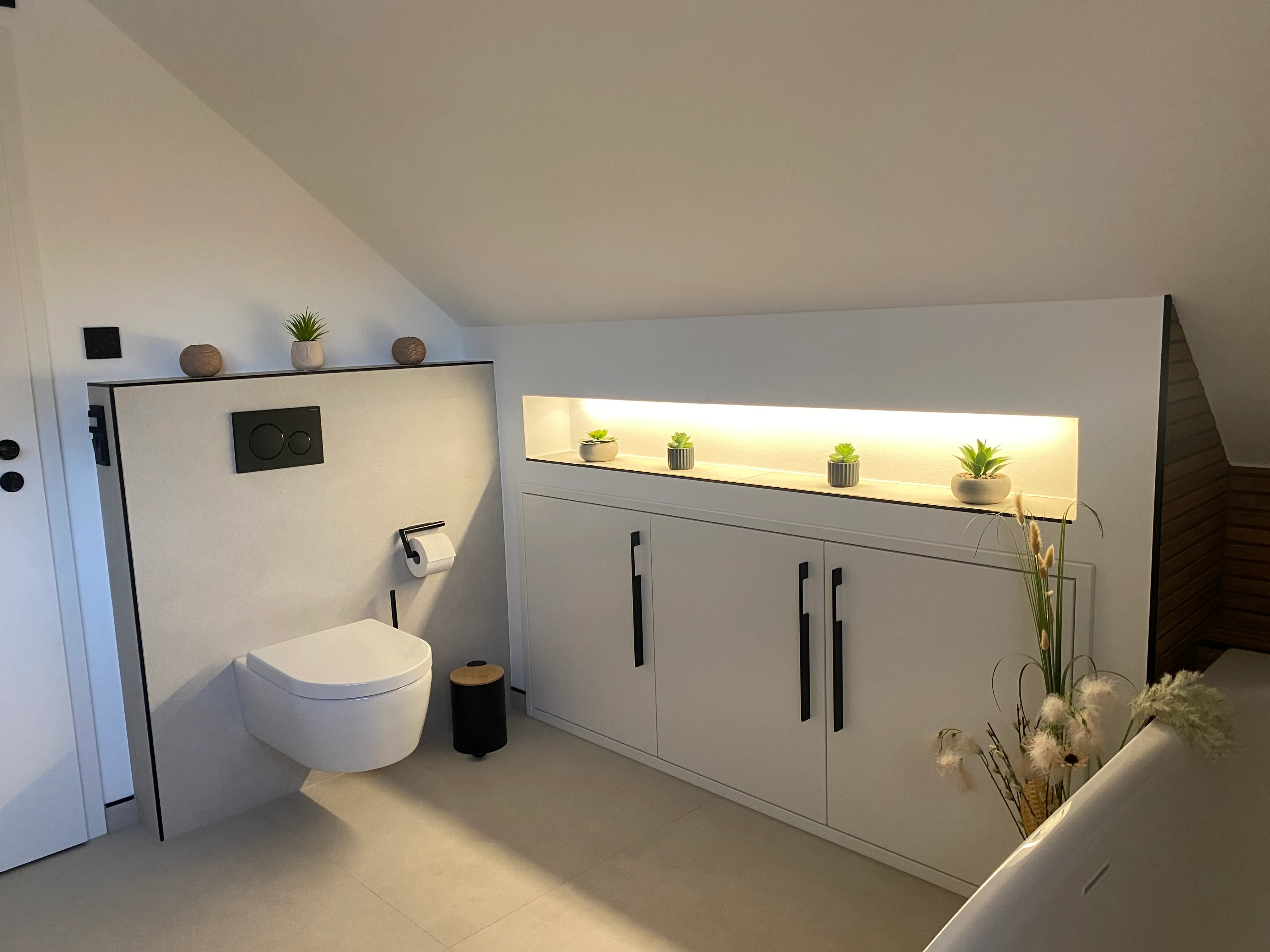 Badsanierung unter Dachschräge mit grauen Fliesen in Betonoptik, Wand-WC und beleuchteter Wandnische