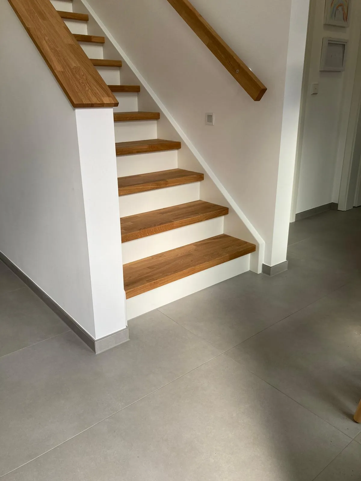 Heller Flur mit grauen Großformatfliesen in Betonoptik und Holztreppe mit gefliester Sockelleiste