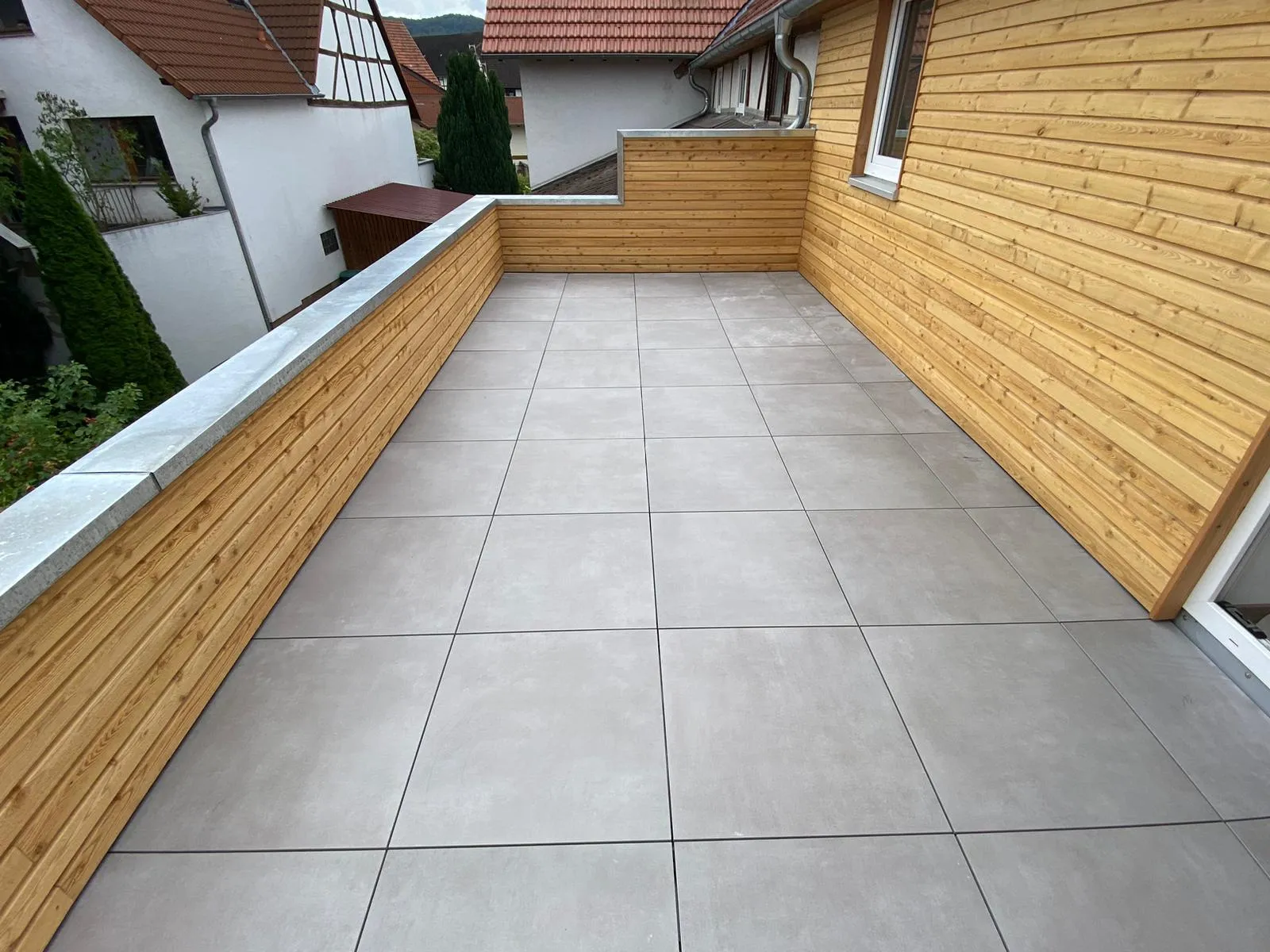 Gefliester Balkon mit grauen Großformatfliesen im Rasterverband und holzverkleideter Brüstung