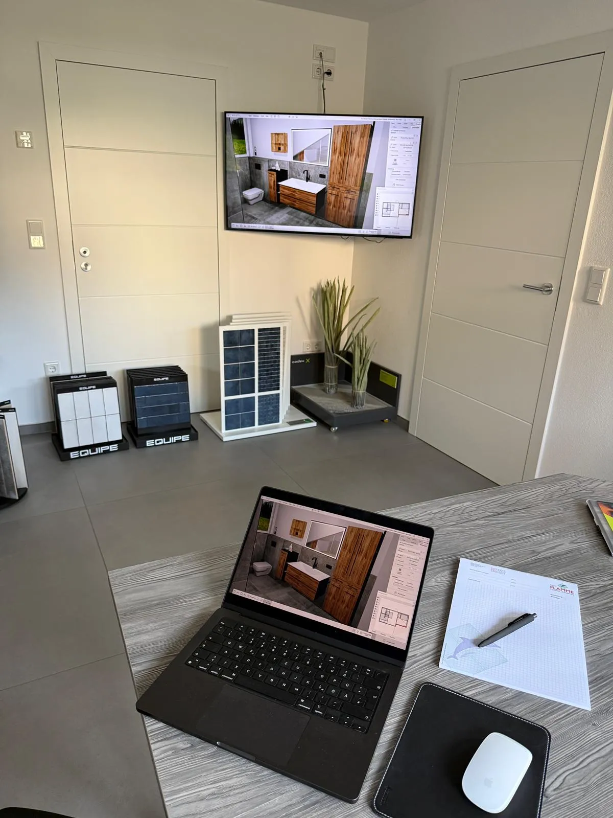 Beratungsraum mit 3D-Badplanung auf Laptop und Wandmonitor, daneben Fliesenmuster im Ausstellungsständer