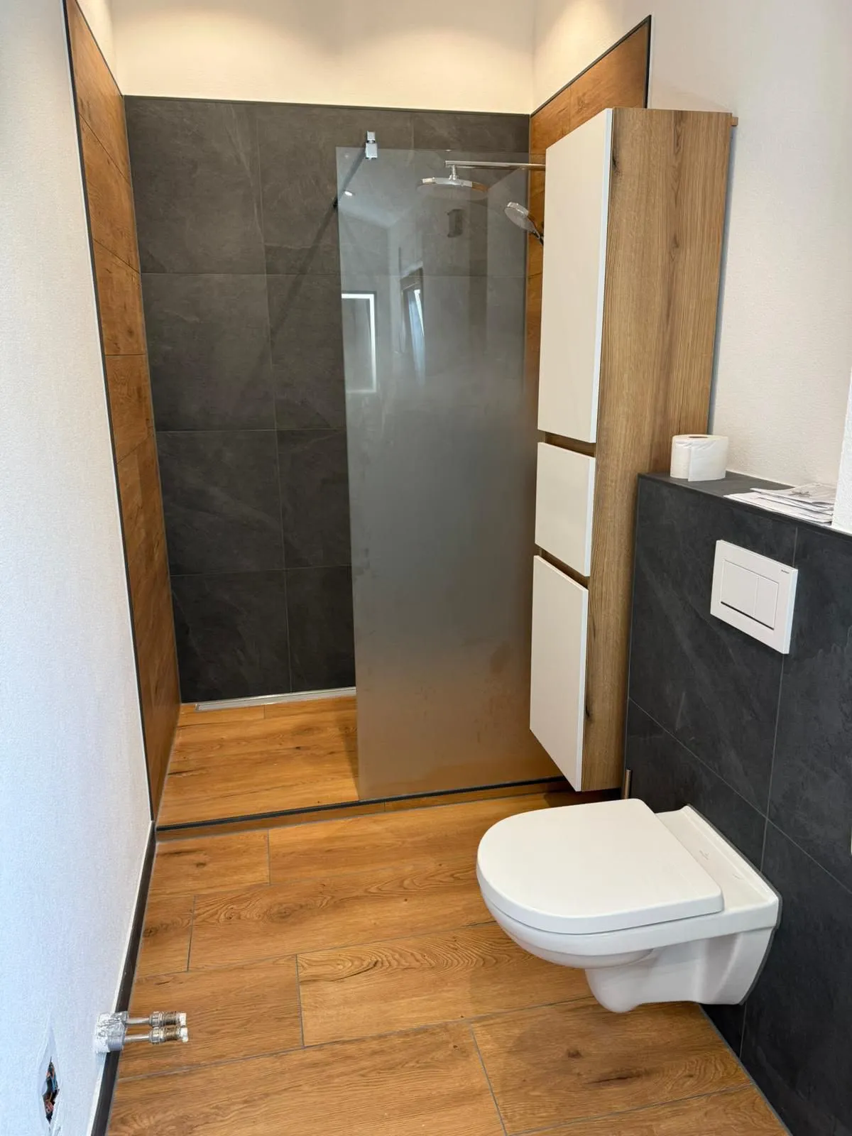 Modernes Bad mit Walk-in-Dusche, dunklen Wandfliesen in Schieferoptik und Bodenfliesen in Holzoptik, Wand-WC und Hochschrank