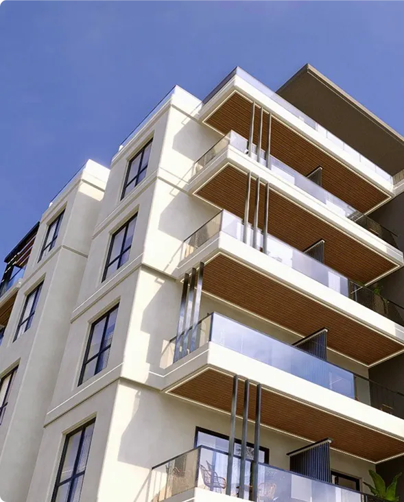 Modern multi-story building with beige walls, black-framed windows, and balconies with glass railings and wood-paneled ceilings.