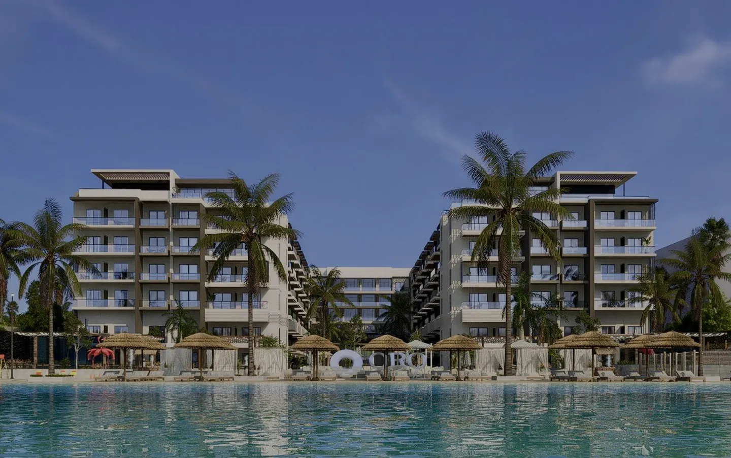 Modern beachfront resort with two six-story buildings, palm trees, thatched umbrellas, lounge chairs, and a large swimming pool in the foreground.