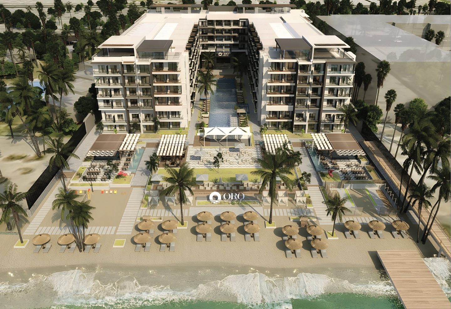 Aerial view of a beachfront resort featuring two six-story buildings flanking a central pool, sandy beach with umbrellas and lounge chairs, palm trees, and a wooden pier extending into the ocean.