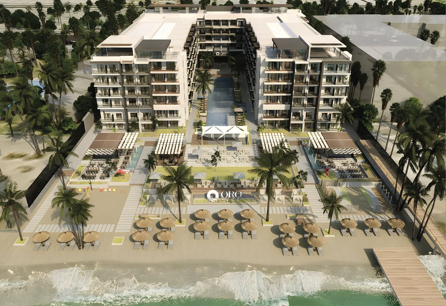 Aerial view of a beachfront resort featuring two six-story buildings flanking a central pool, sandy beach with umbrellas and lounge chairs, palm trees, and a wooden pier extending into the ocean.