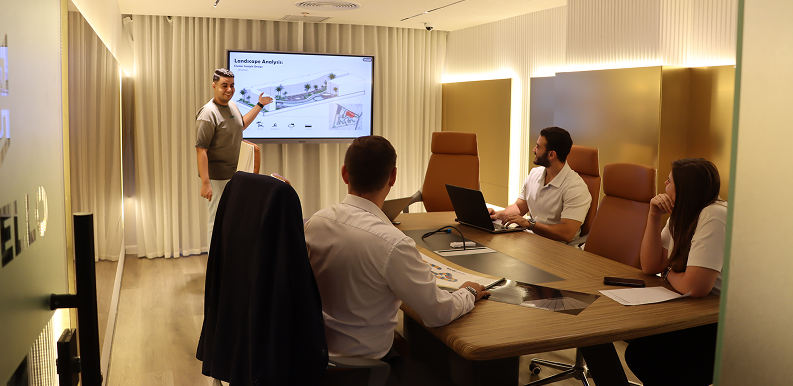 Man presenting landscape design on screen to three coworkers seated around a conference table.