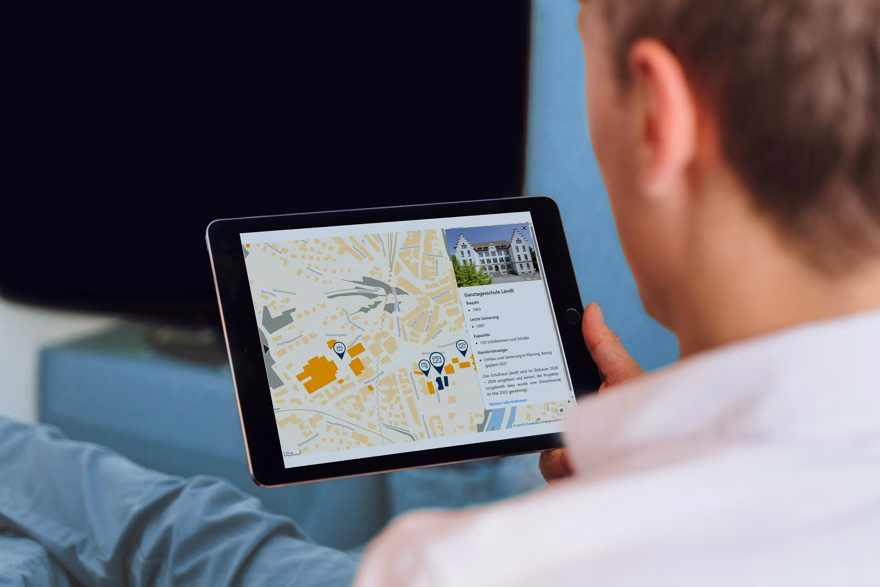 Person hält Tablet mit interaktiver Stadtkarte und Details zur Ganztagesschule Ländli.