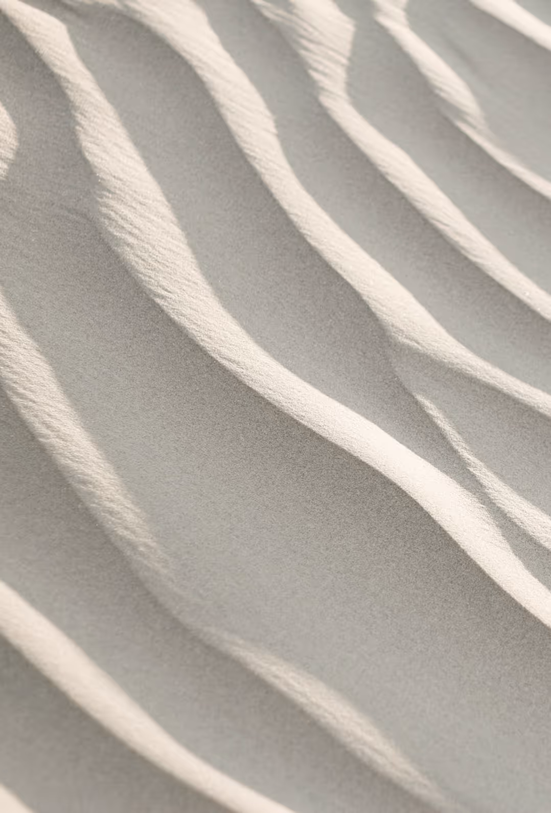 Close-up of light beige sand with soft, flowing ripple patterns.