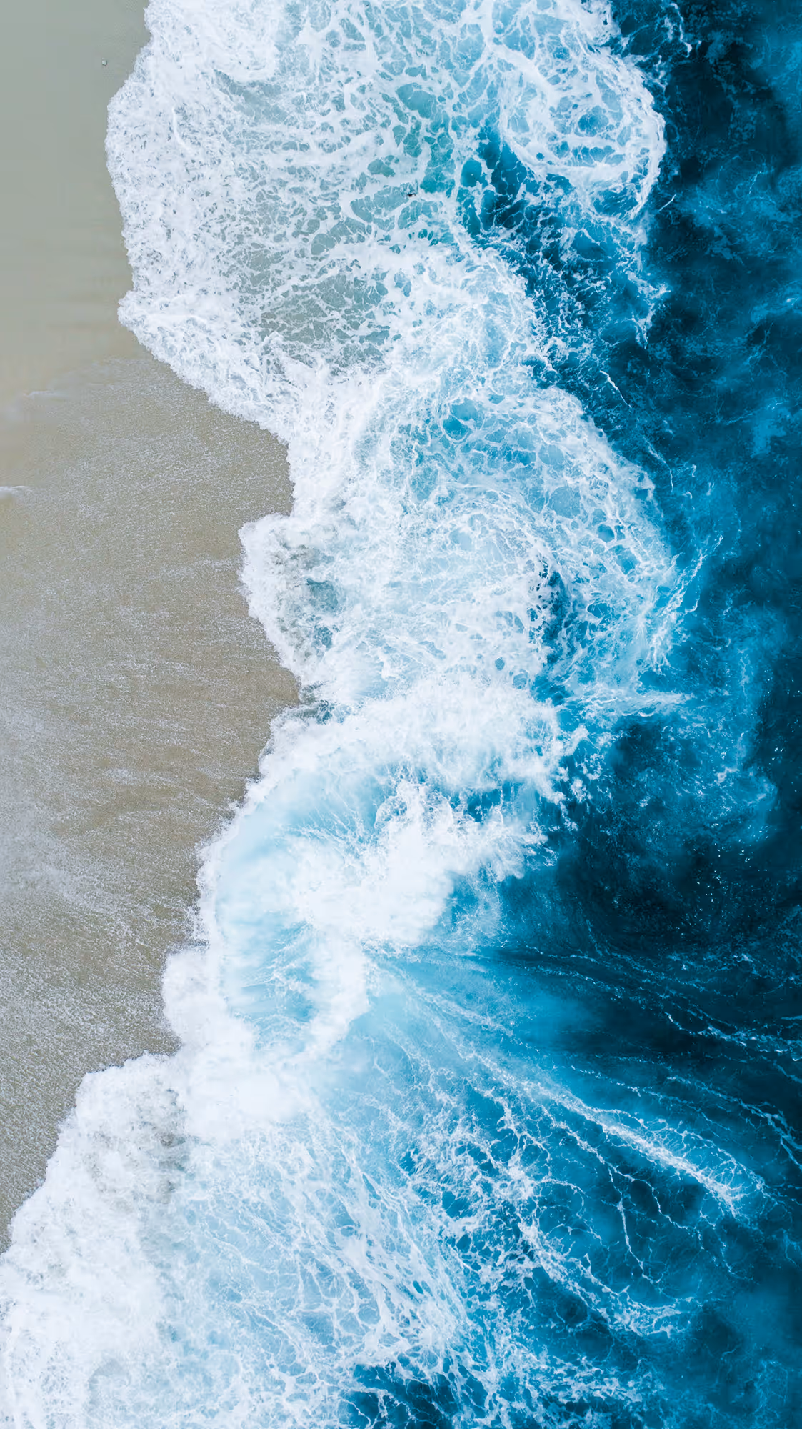 Aerial view of ocean waves crashing onto a sandy beach with white seafoam.