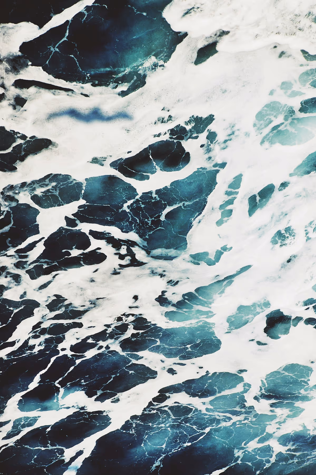 Close-up aerial view of dark ocean water with white sea foam and waves.