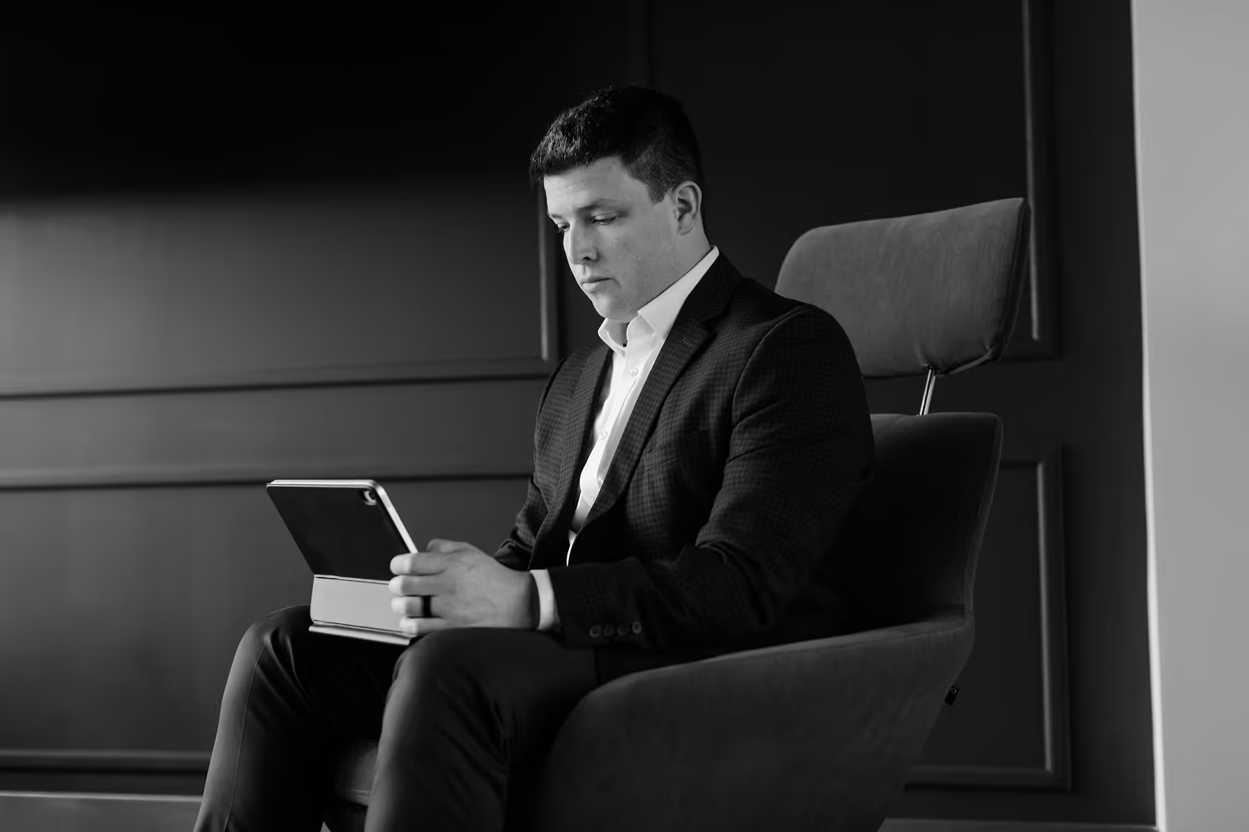 Man in suit sitting in chair and looking at a tablet device.