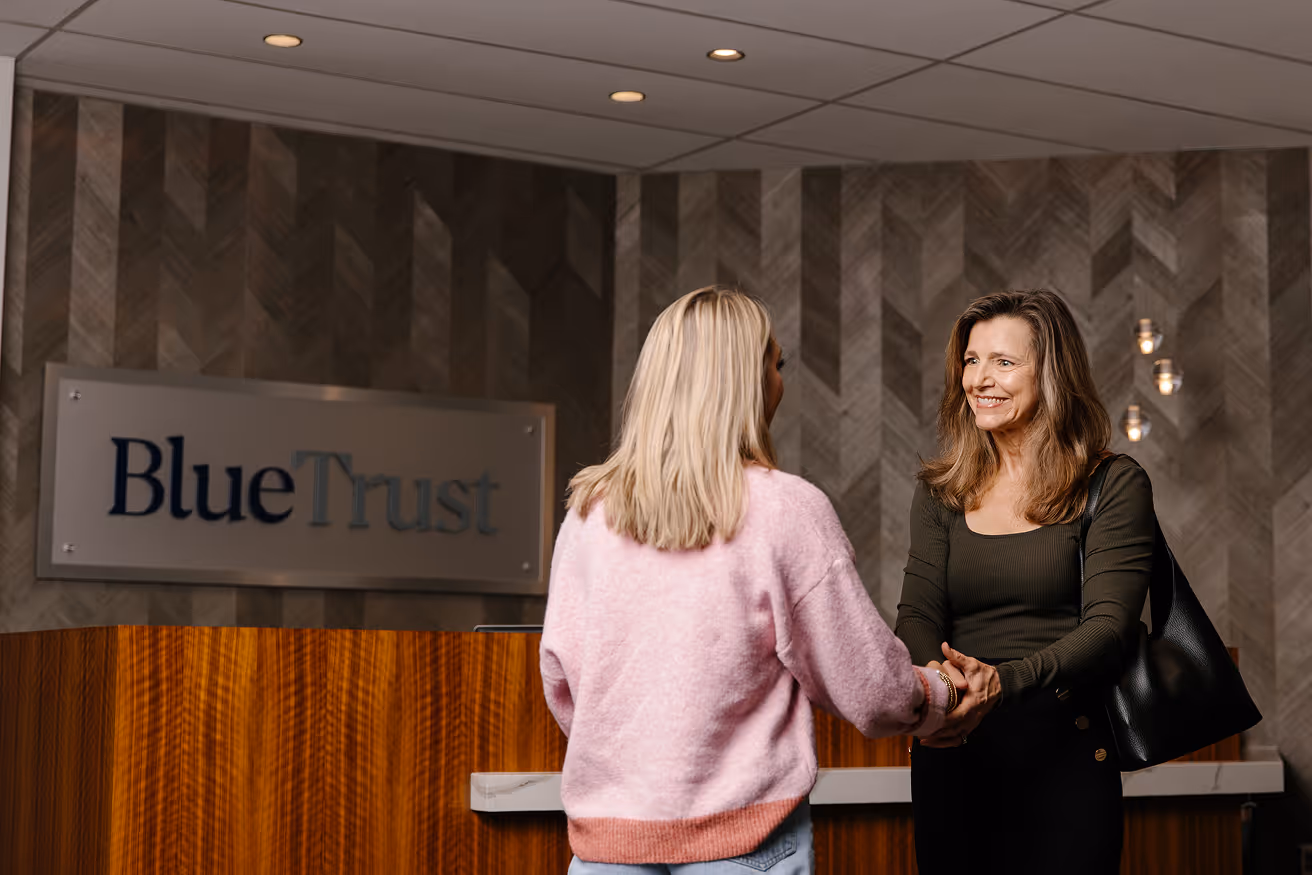 Two women shaking hands in a BlueTrust office lobby with wood and patterned walls.