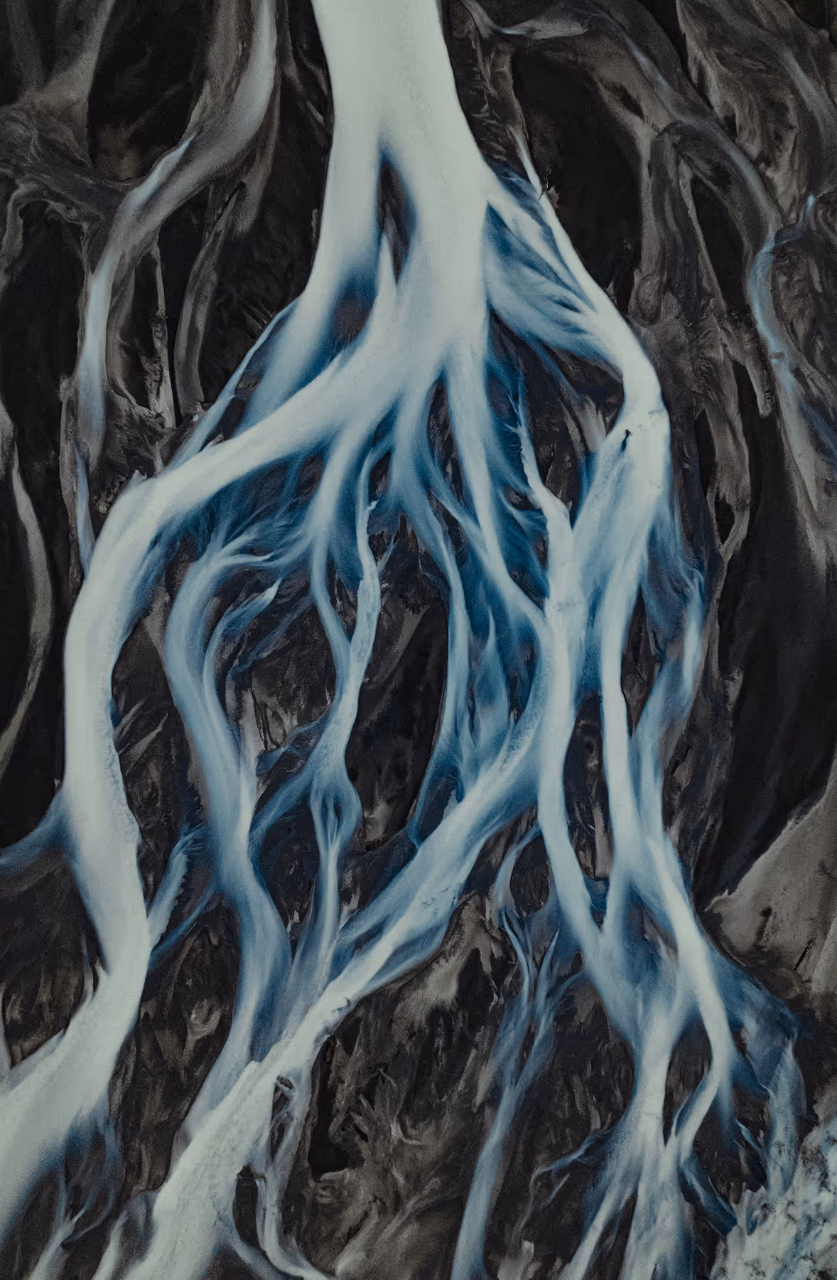 Aerial view of winding icy blue river streams branching through dark terrain.