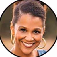 Smiling woman with short curly hair and gold hoop earrings in outdoor light.
