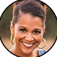 Smiling woman with short curly hair and gold hoop earrings in outdoor light.