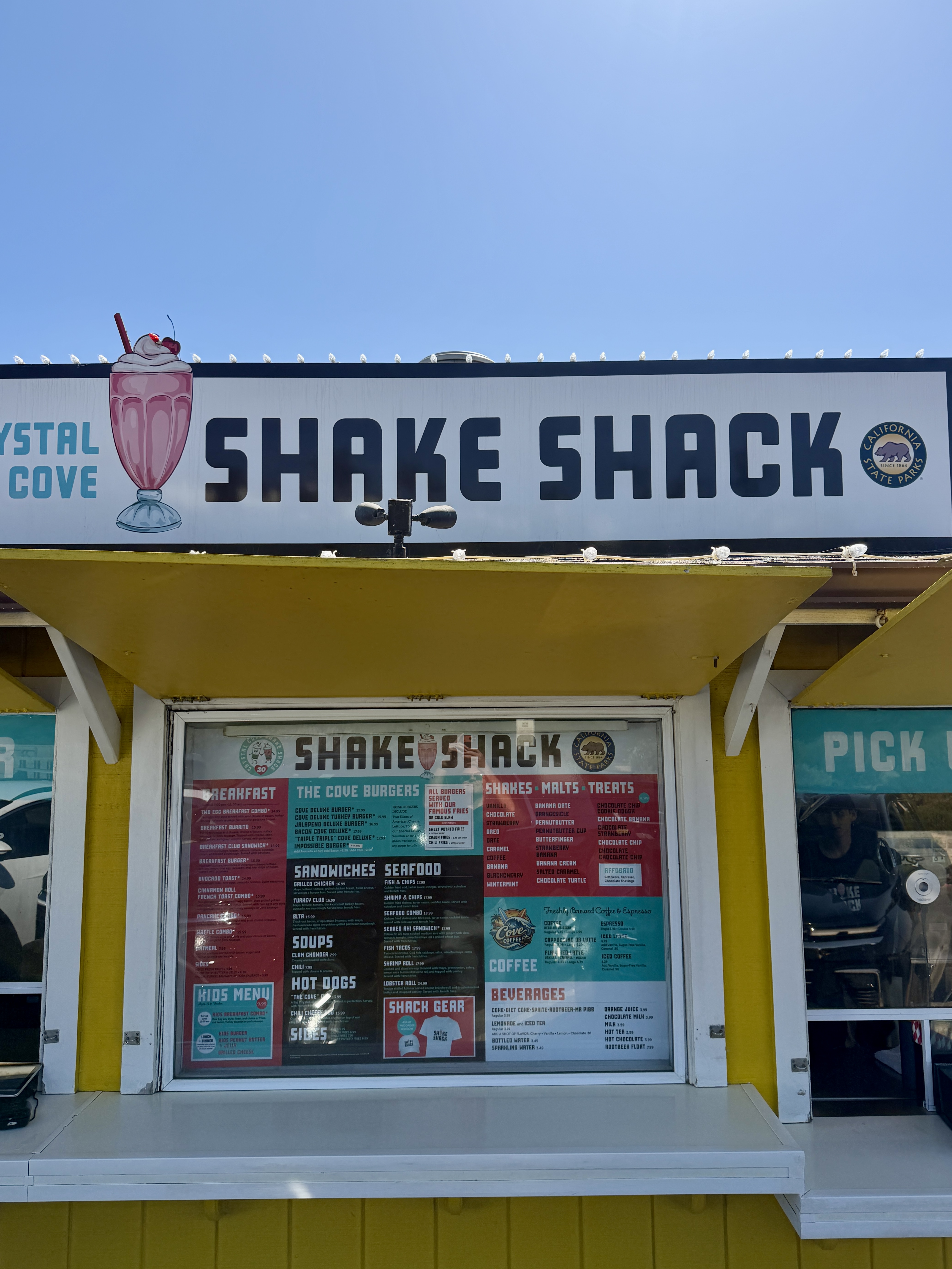 Crystal Cove Shake Shack storefront on Pacific Coast Highway — yellow walk-up counter with vintage milkshake sign and posted menu in Newport Coast