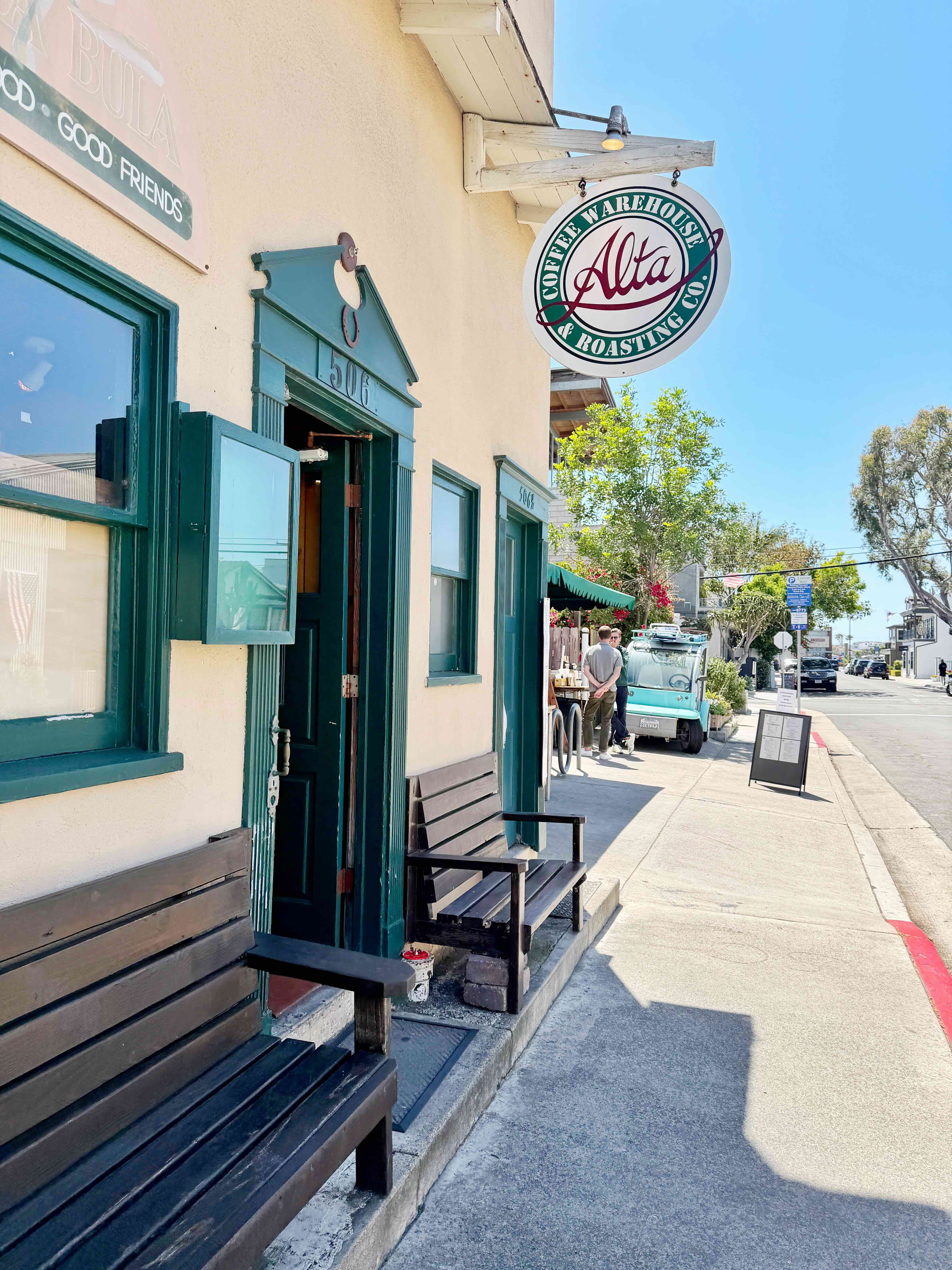 Alta Coffee storefront in Newport Beach Cannery Village — green window trim, exterior wooden bench, and the round Alta Coffee Warehouse & Roasting Co. sign on a sunny day