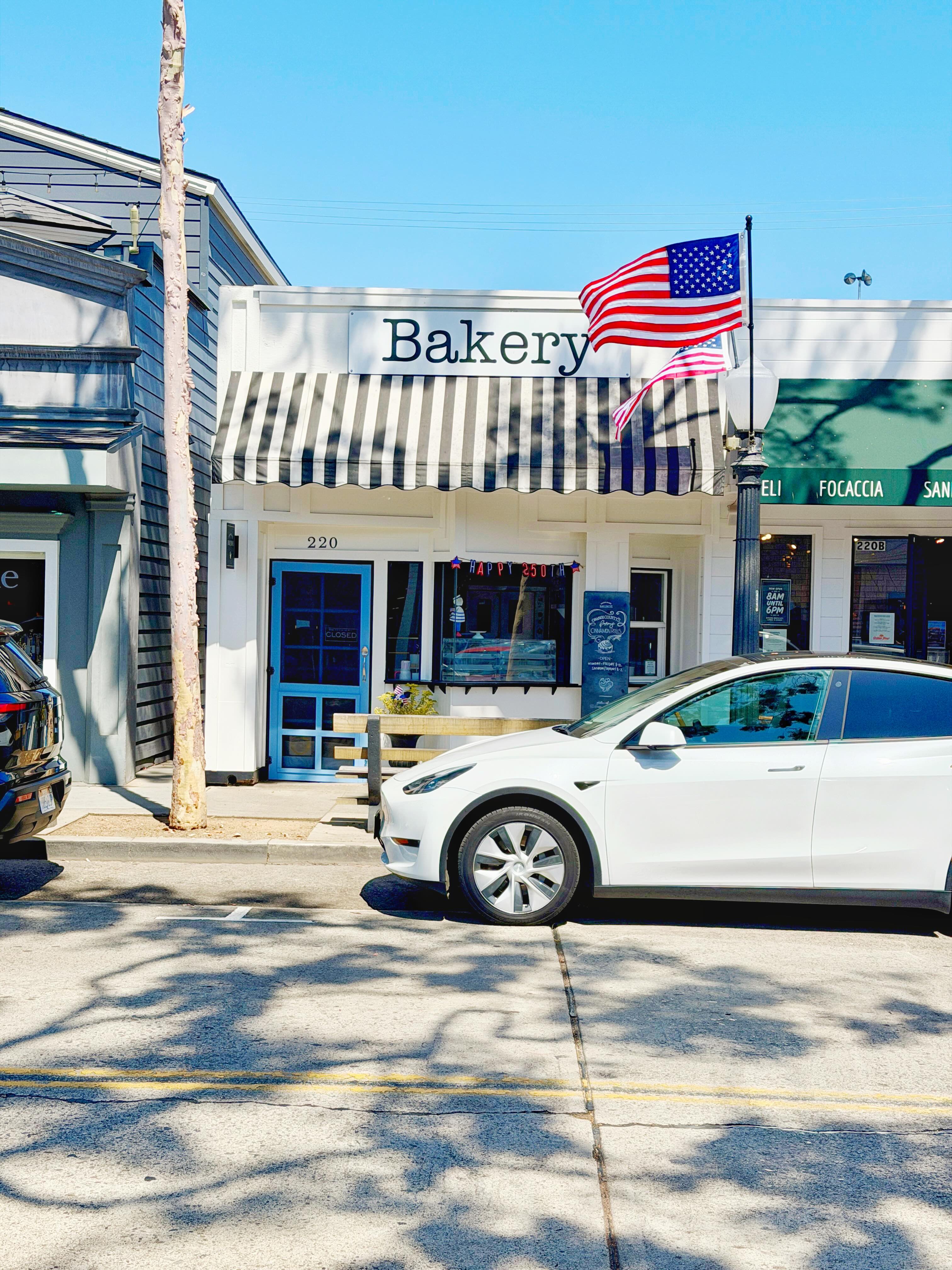 Balboa Island Baking Company storefront at 220 Marine Avenue — navy and white striped awning, American flag flying, blue door, on a sunny Newport Beach morning