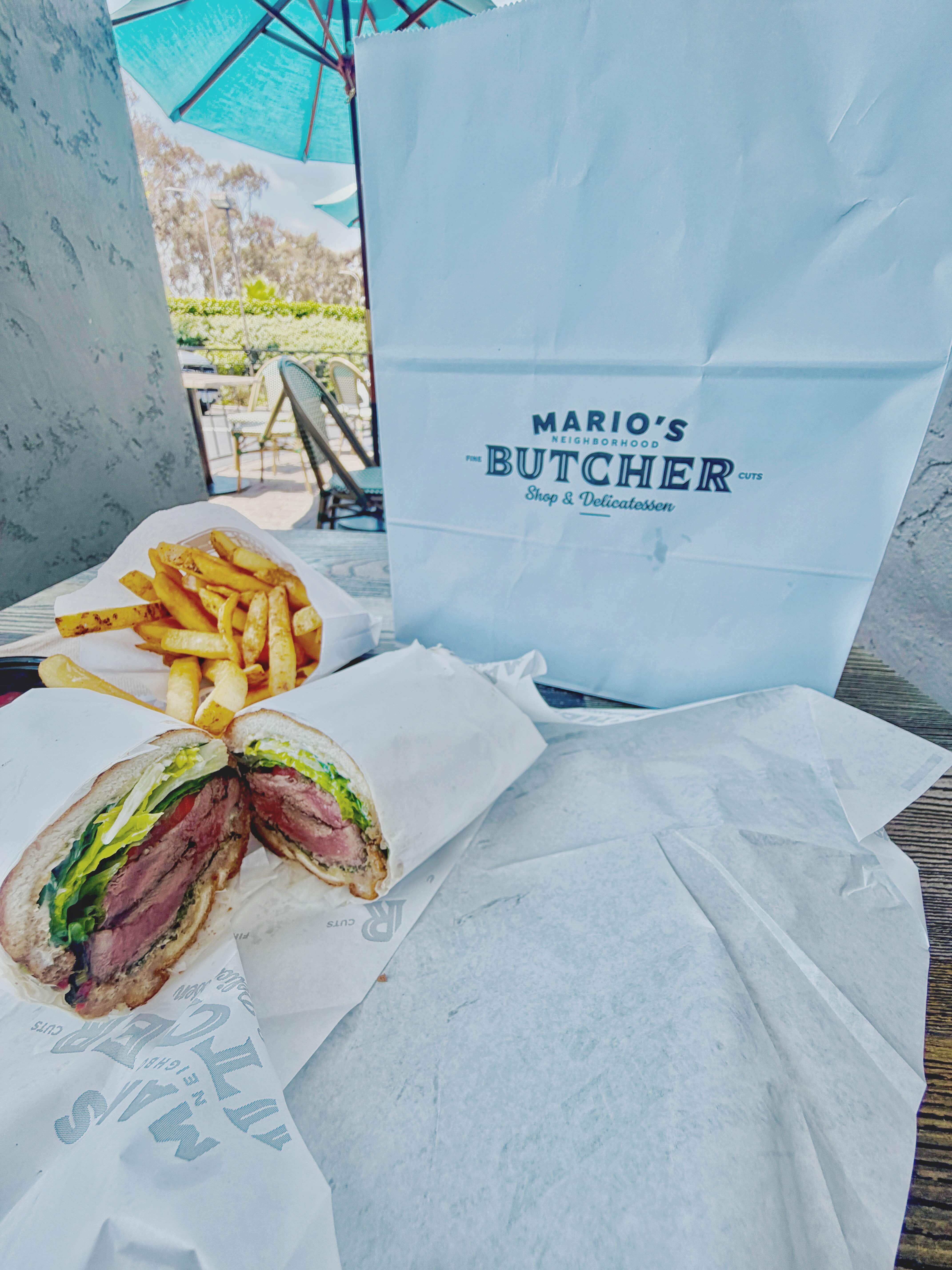 Mario's Butcher Shop steak sandwich and fries on an outdoor table with the branded takeout bag and Mario's wordmark visible beside it