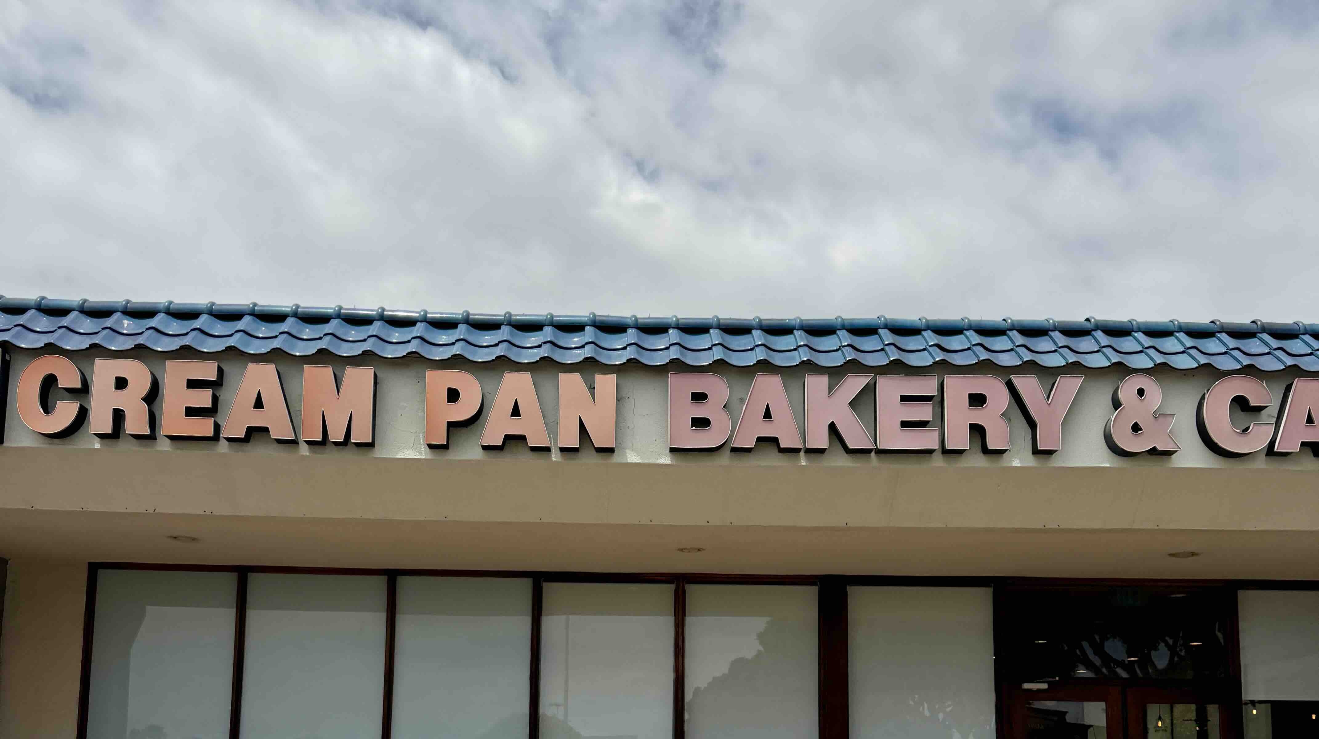 Cream Pan Bakery & Cafe storefront in Old Town Tustin. Copper-colored channel letters spell out 'CREAM PAN BAKERY & CAFE' across a blue Spanish-tile roof line above a beige stucco facade with large display windows and glass entry doors.