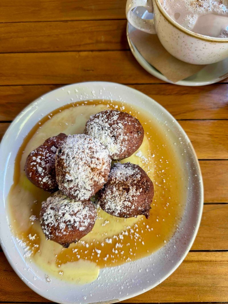 Beignets dusted with powdered sugar over cream sauce and caramel drizzle at Ramos House Cafe, served with a cappuccino.