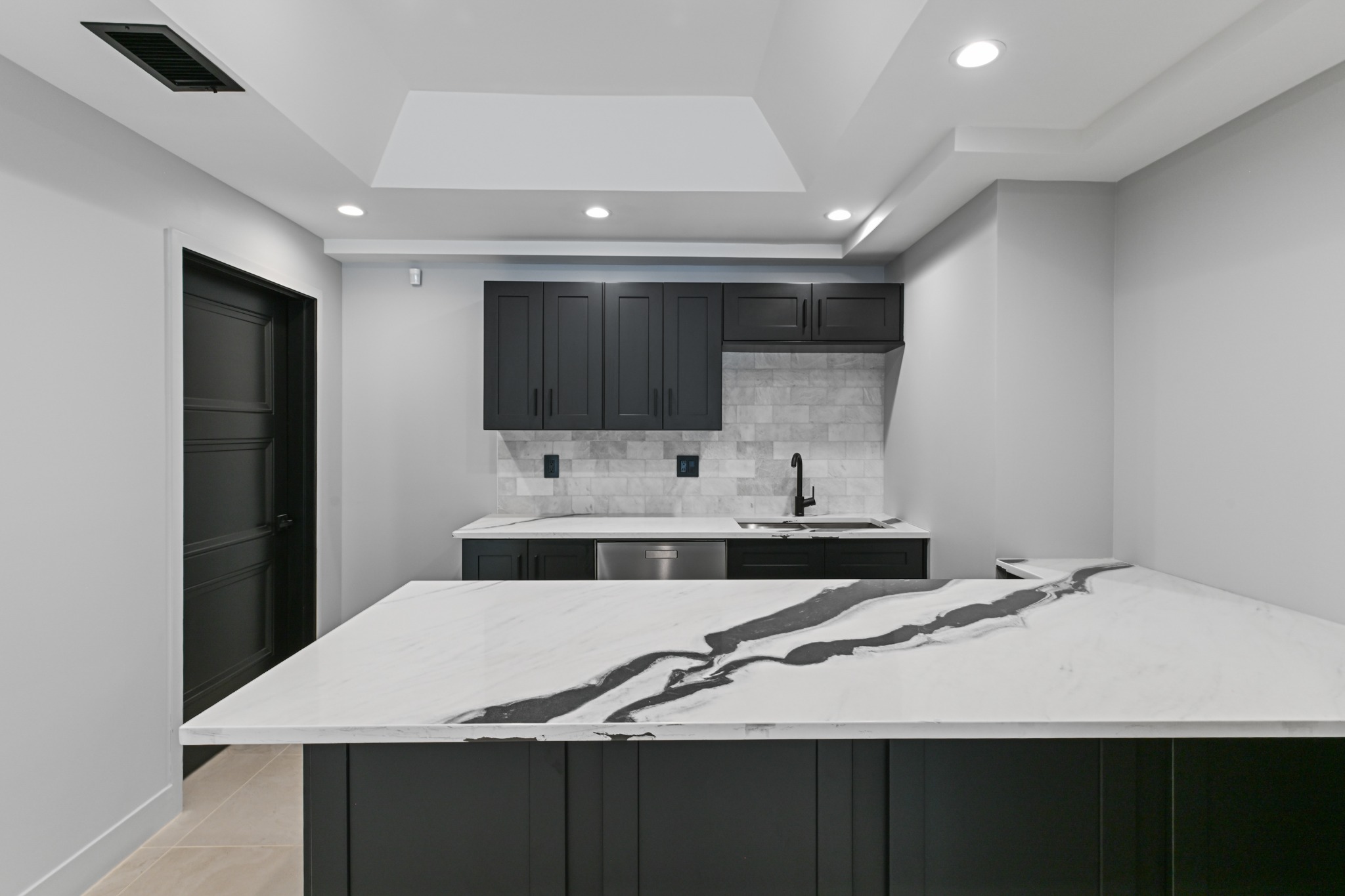 Finished basement bar with black cabinetry, marble-look counters, and tray ceiling