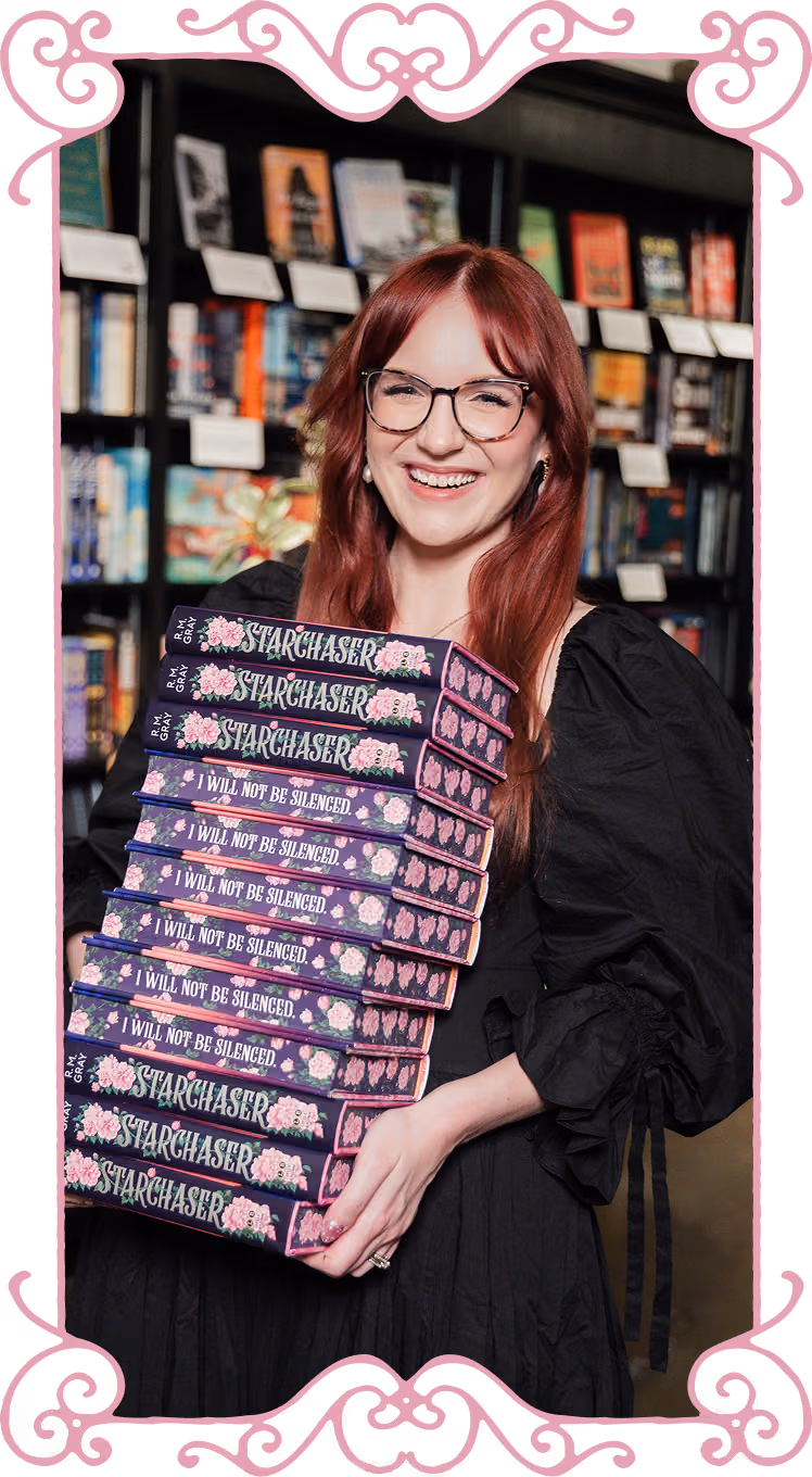 R.M. Gray holding a stack of books titled Starchaser and I Will Not Be Silenced.