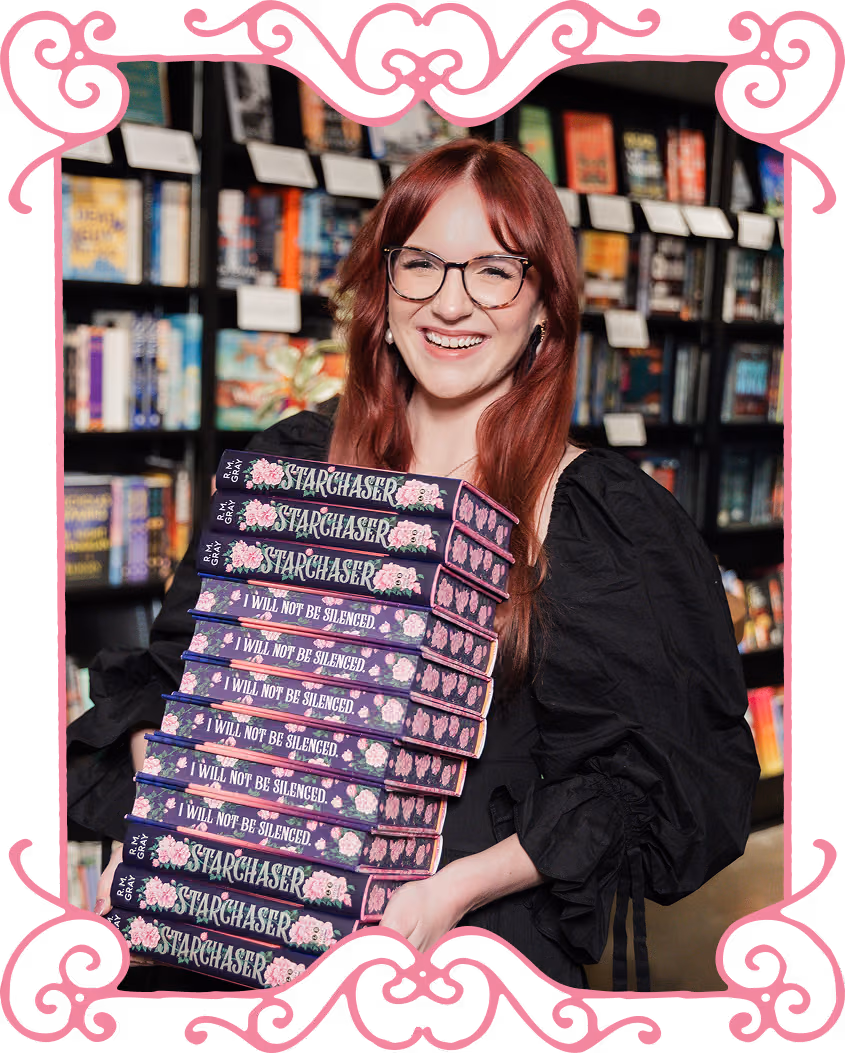 R.M. Gray holding a stack of books titled Starchaser and I Will Not Be Silenced.