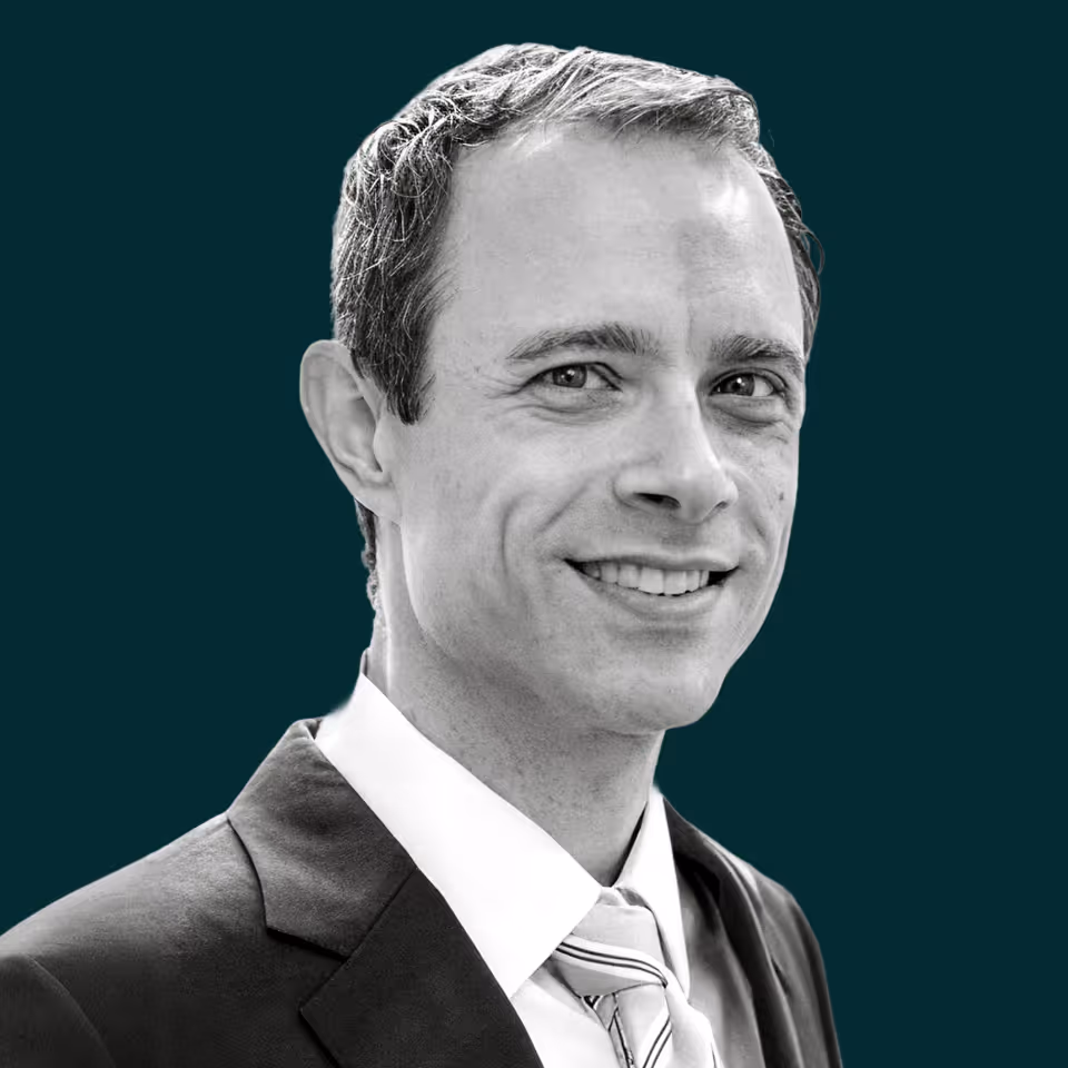 Smiling man wearing a suit and striped tie against a dark teal background.