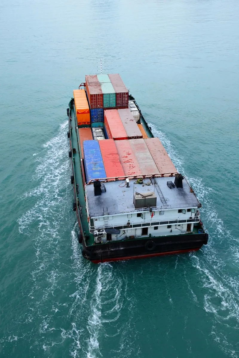 Cargo ship sailing on calm blue water carrying stacked colorful shipping containers.