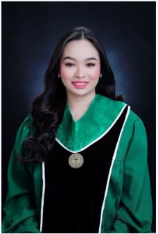 Young woman with long dark hair wearing a green and black graduation gown with a medallion, smiling against a dark background.