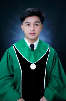 Young man in green and black graduation gown with a medallion on a dark blue background.