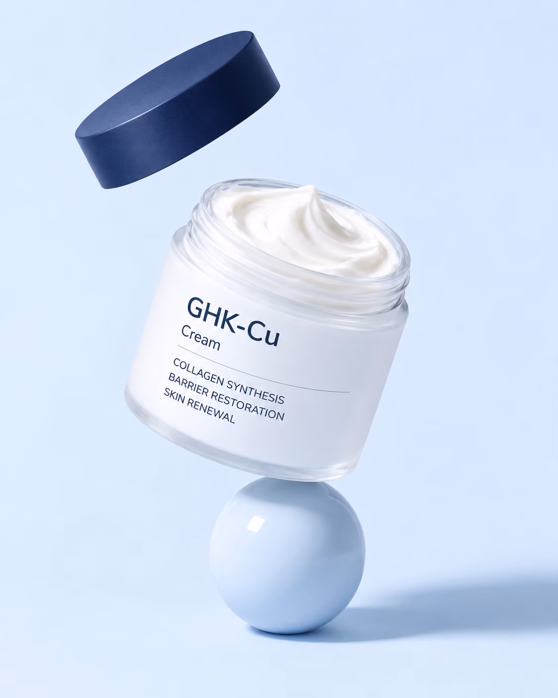 Open jar of GHK-Cu Cream beside its navy lid and a swipe of white cream on a white plinth against a navy wall