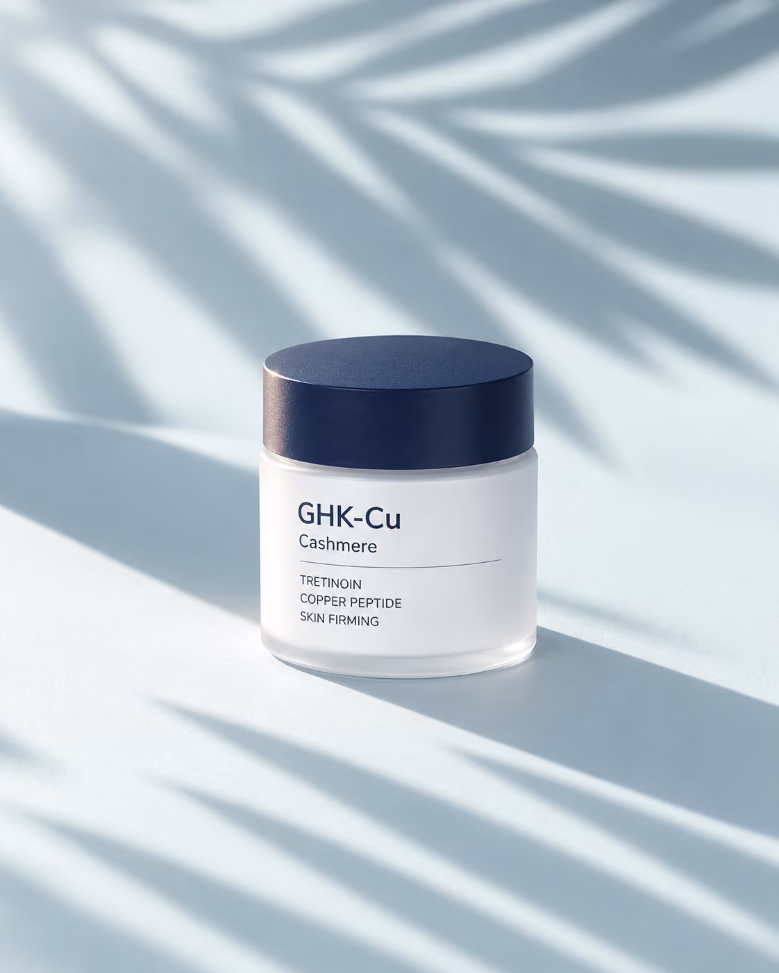 GHK-Cu Cashmere cream jar with a navy lid on a camel surface under palm leaf shadows
