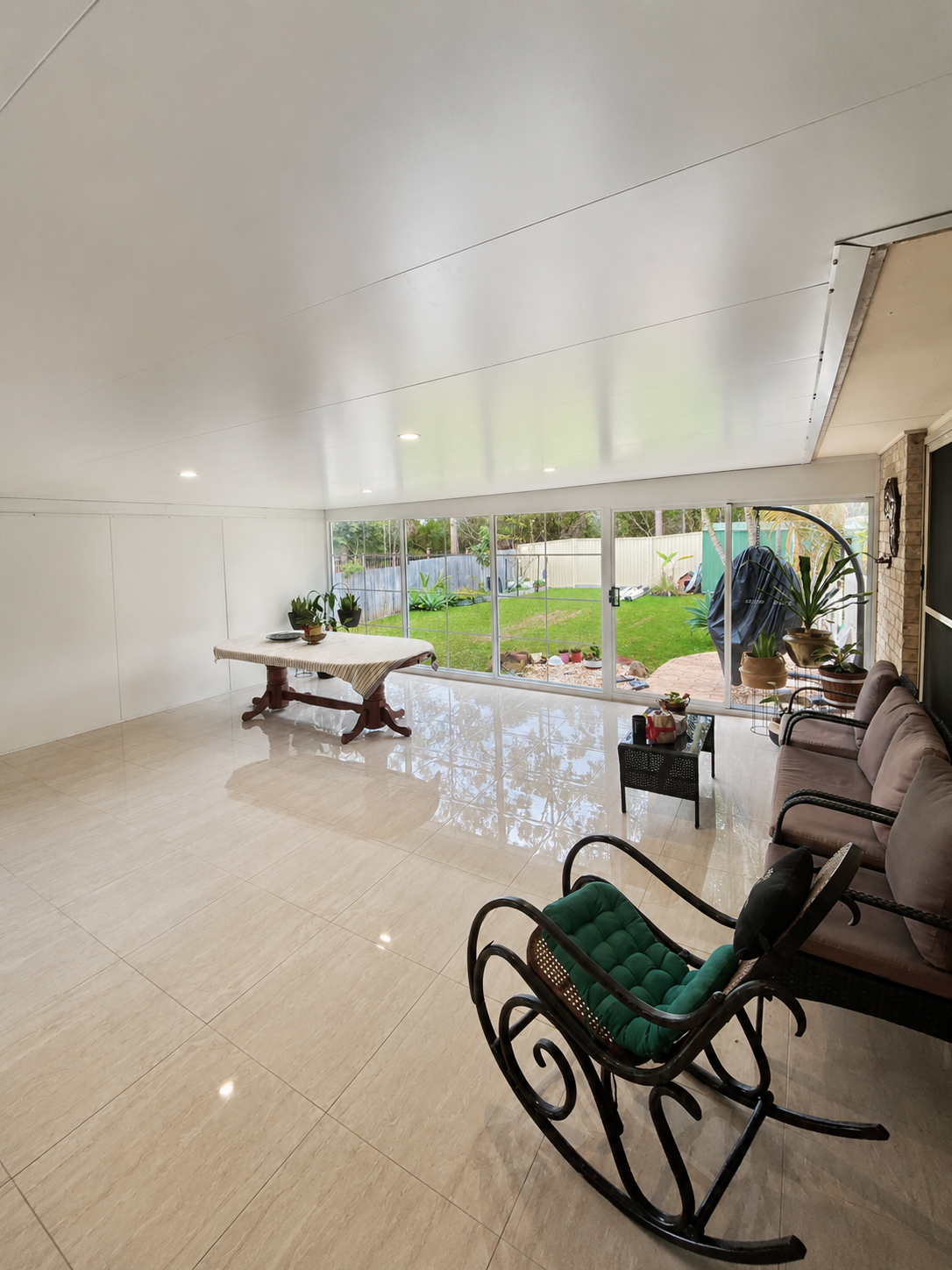 Sunroom-style room enclosure with full-height glass windows opening onto the yard.