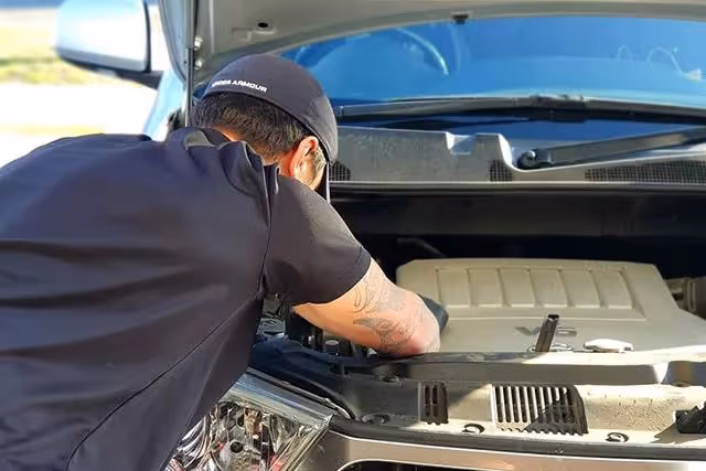 Mechanic performing a logbook service on a vehicle engine bay in a Masterton workshop