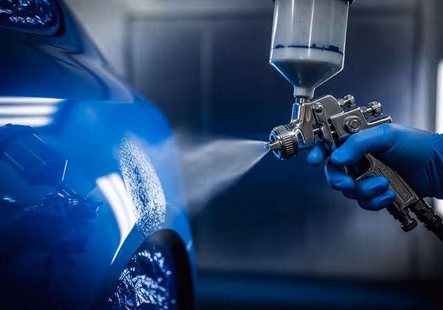 Spray gun painting a car panel in a professional paint booth