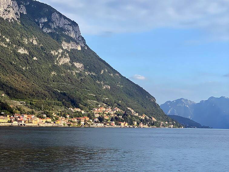 Lakeside village below steep green mountains on Lake Como, Italy