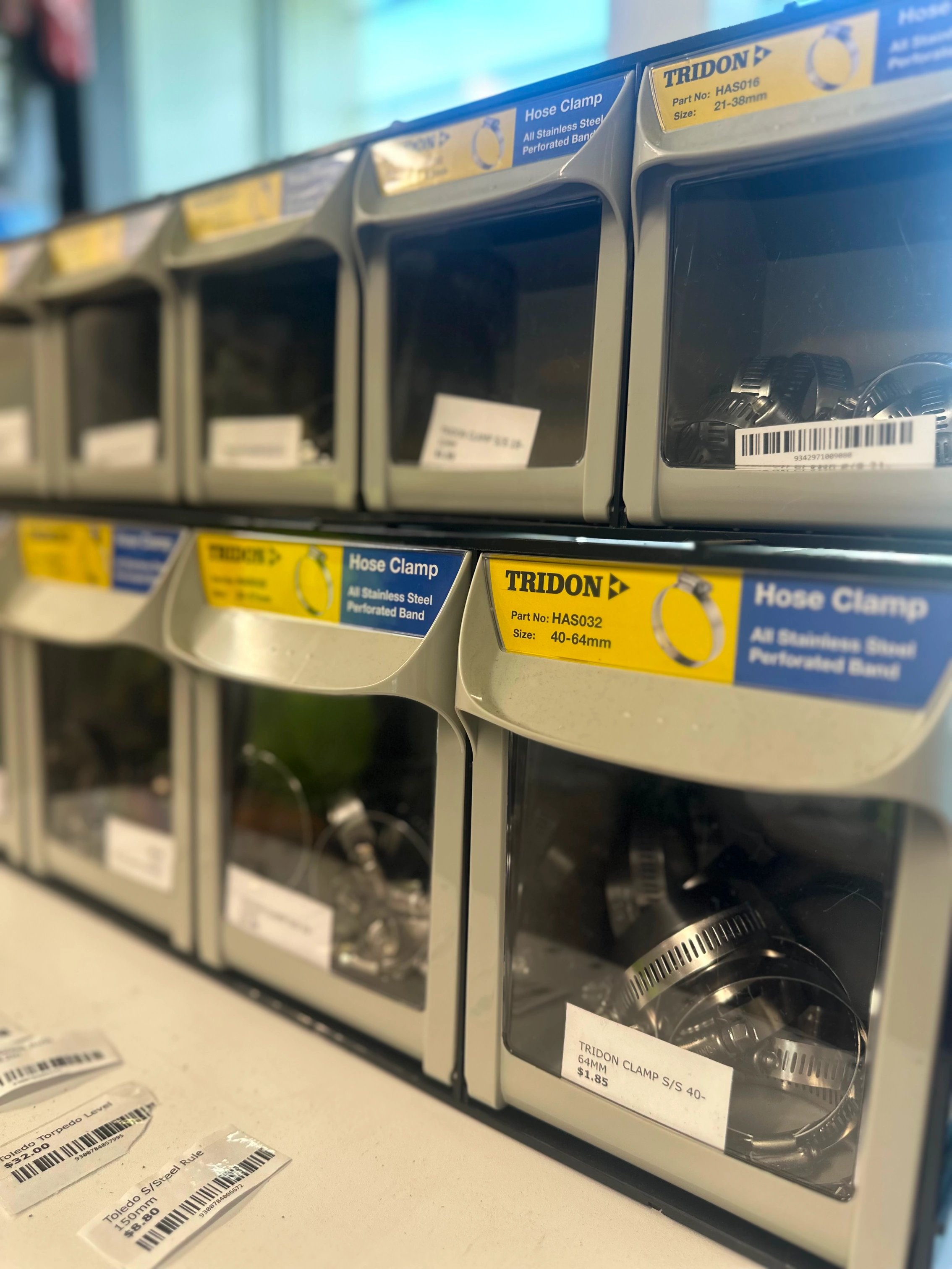 Storage bins containing various sizes of stainless steel hose clamps, labeled with part numbers and sizes.