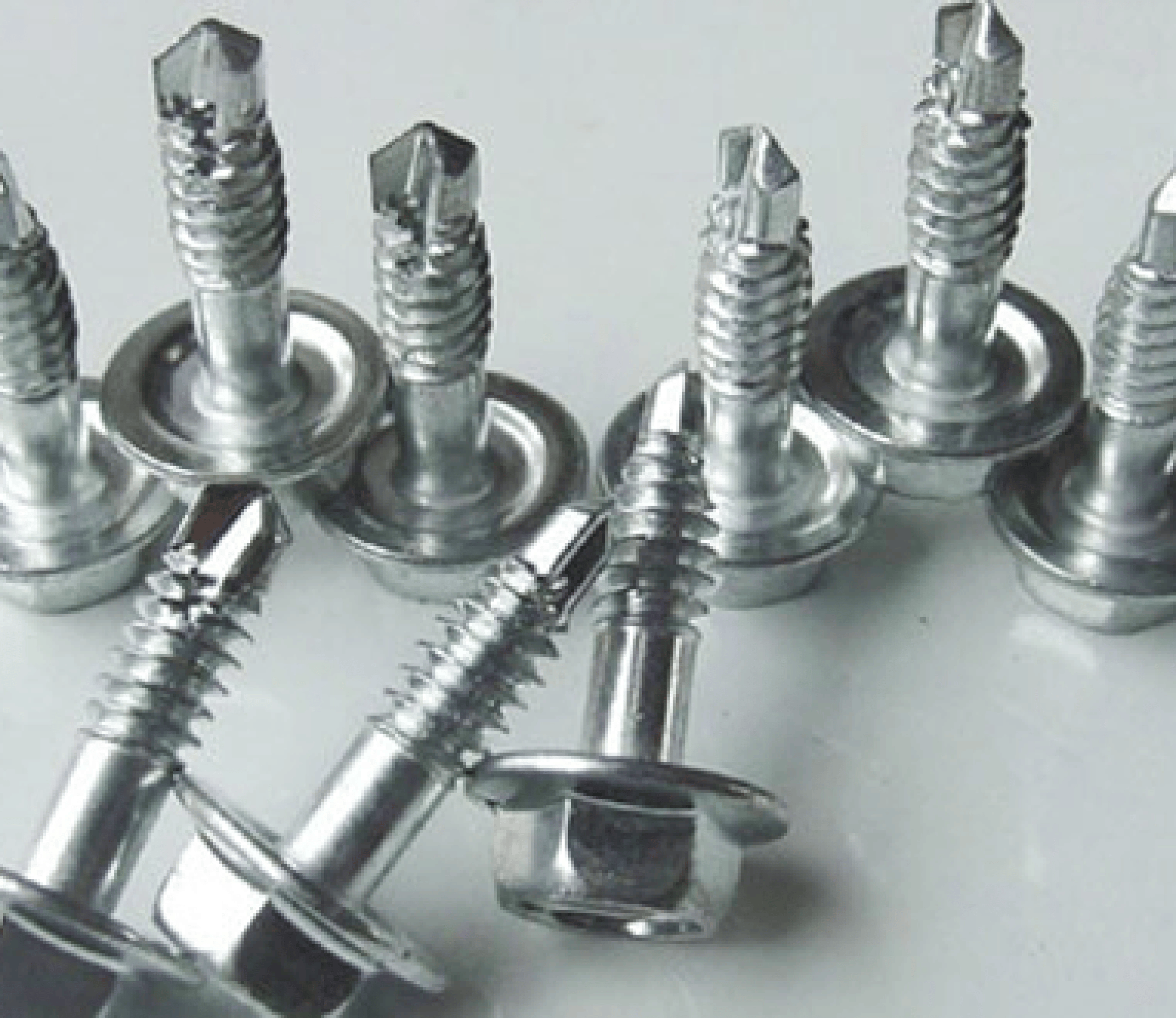 Close-up of several shiny silver self-drilling metal screws with hex washer heads on a light background.