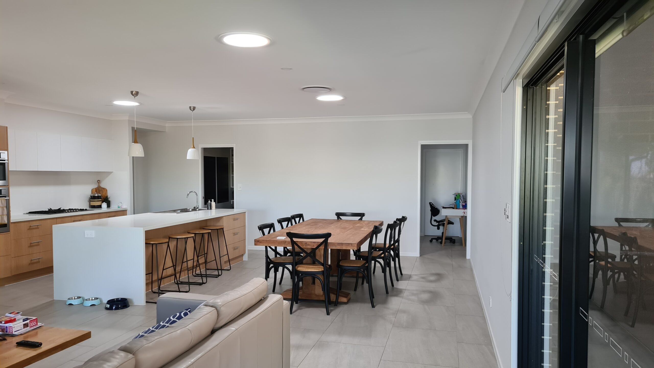 Modern open kitchen and dining area with a wooden dining table surrounded by black chairs, a kitchen island with bar stools, and a sliding glass door.